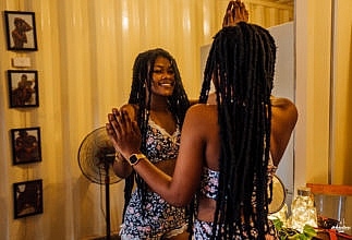 Image of a woman wearing long braids looking at herself in the mirror and smiling
