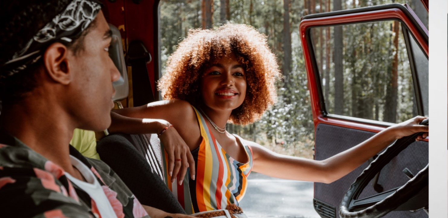A Black woman with curly hair smiles from the front seat of a Jeep.